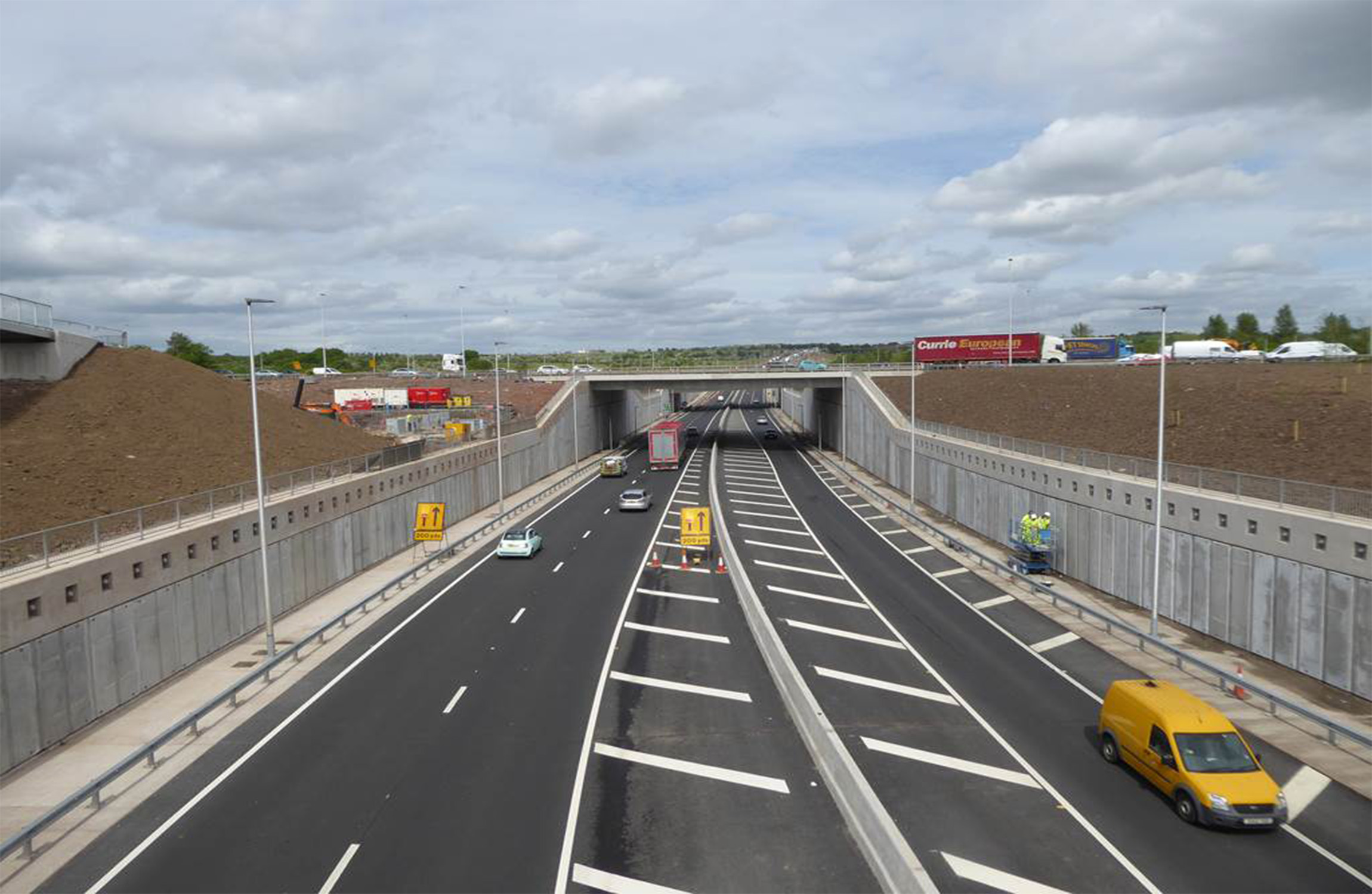 Multiple vehicles driving down a newly constructed motorway that runs under a bridge.