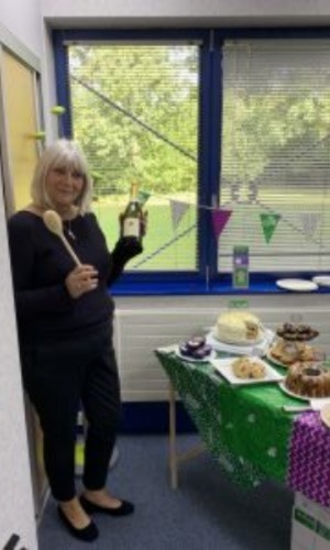 A woman holding a bottle of champagne standing next to a bake sale table.