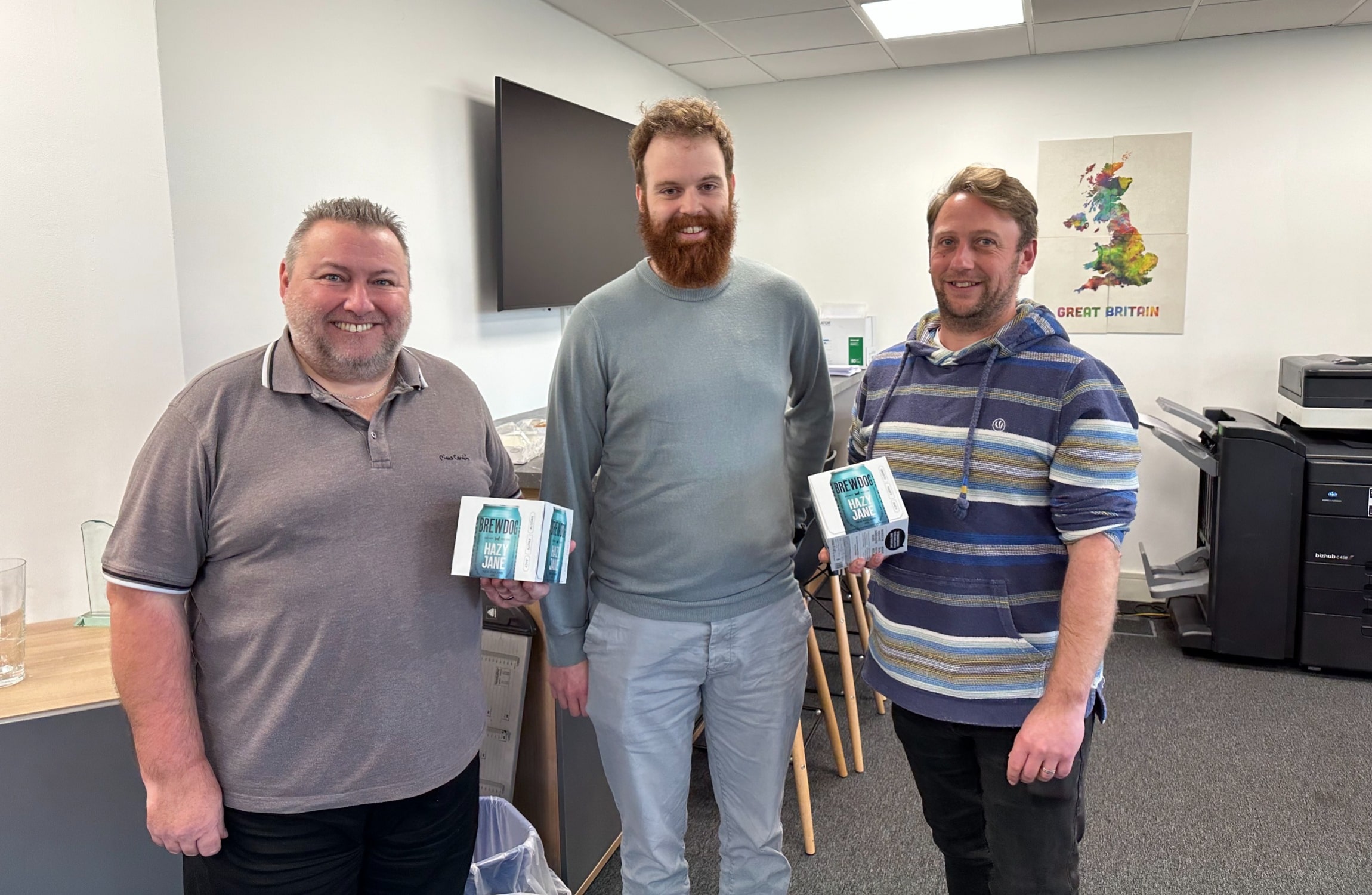 Three men stood in an office with two of them holding a prize they won from a quiz.