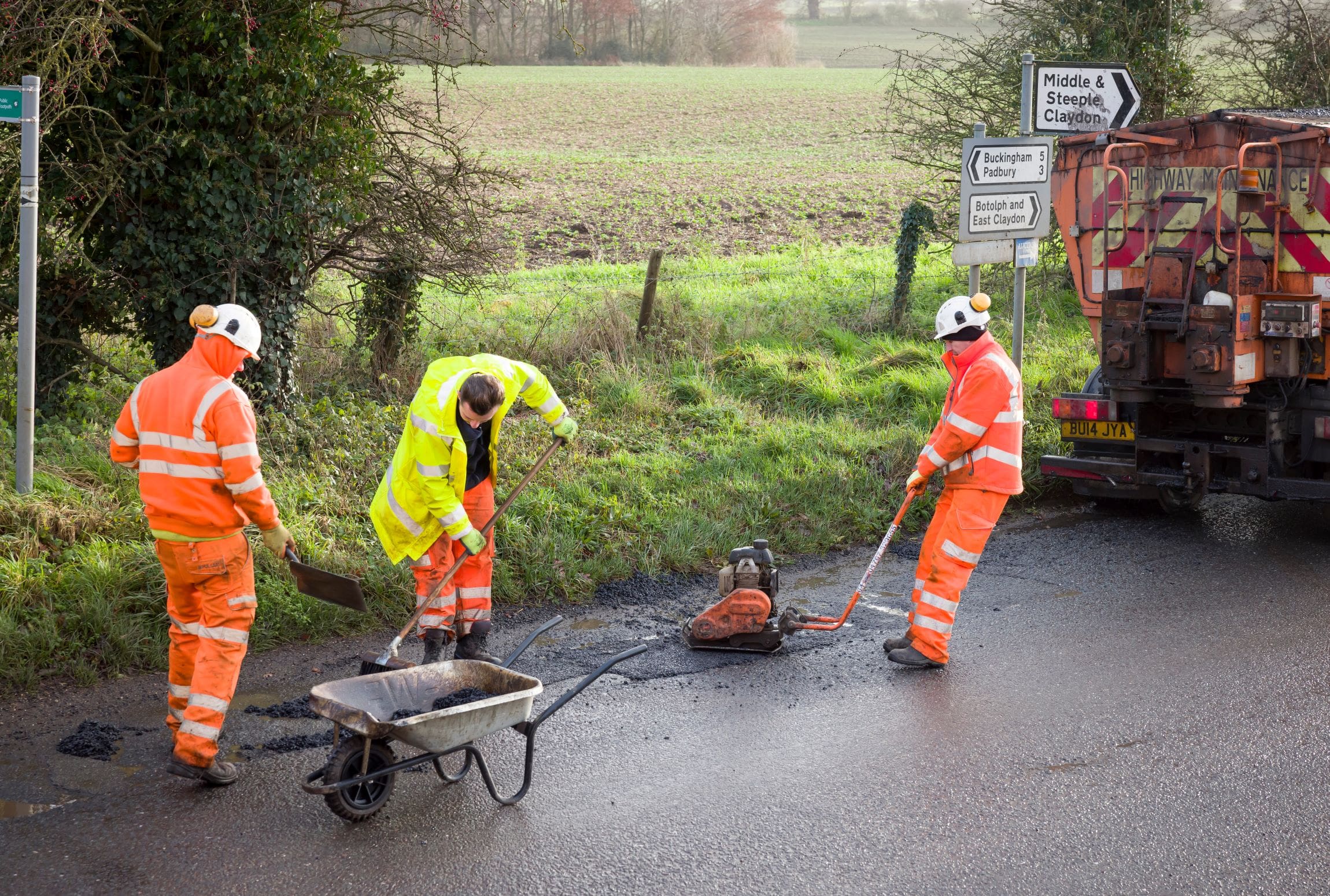 Road works, road crew team, men wearing high visibility hi vis orange clothing. Repairing potholes in a rural country road