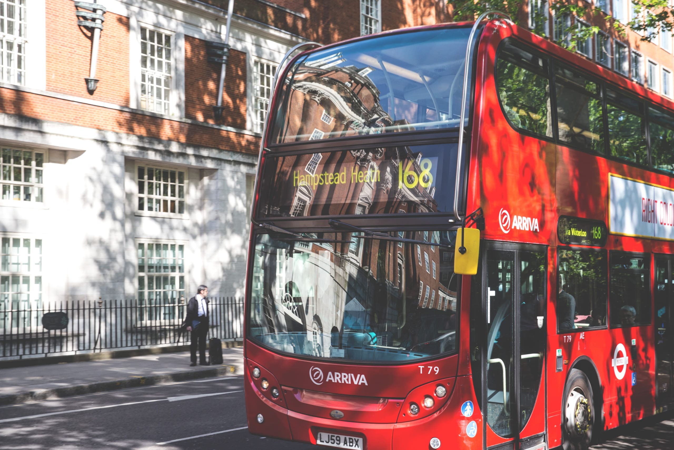 A red bus at a stop in a street of London.