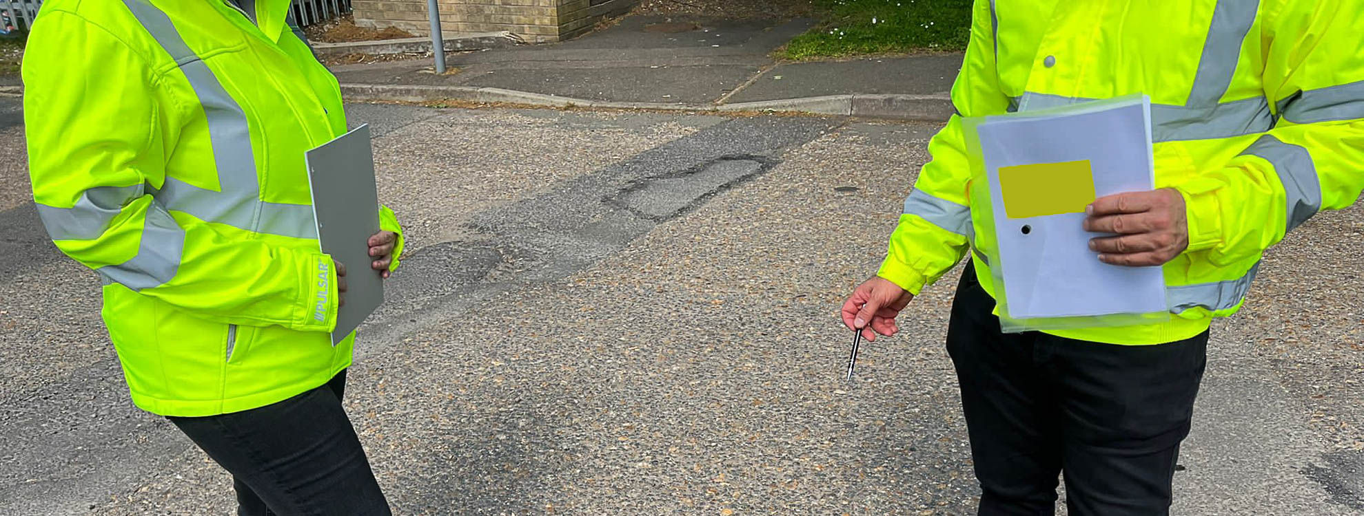 Two TMS road safety Inspectors inspecting a large pothole in the road.