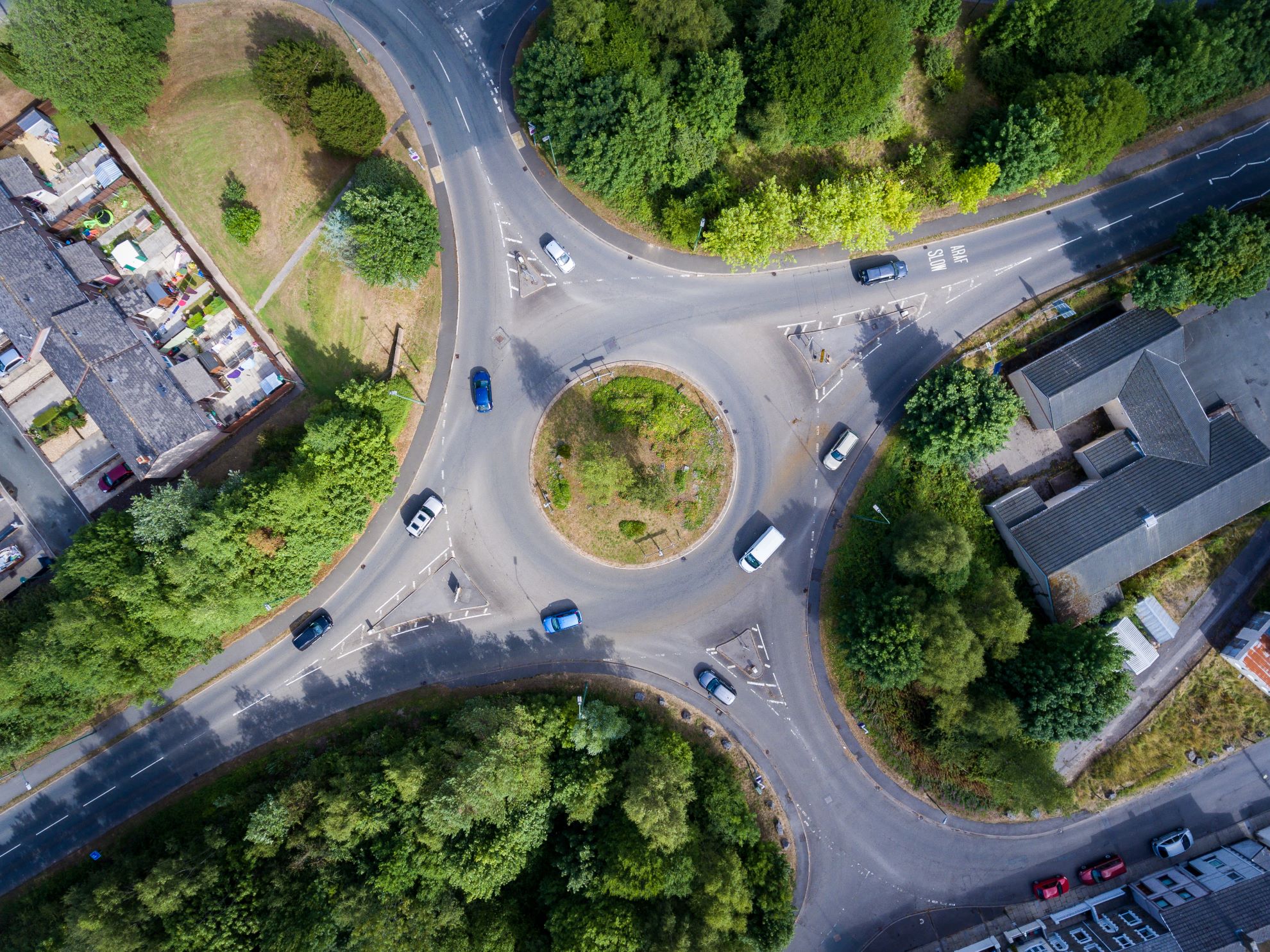 A roundabout with four exits surrounded by lots of greenery and trees.