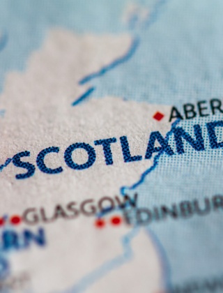 A close up view of a map of Scotland with a red pin sticking in it.