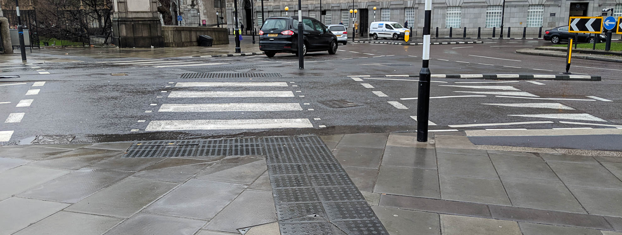 A zebra crossing next to a roundabout in a busy city centre.