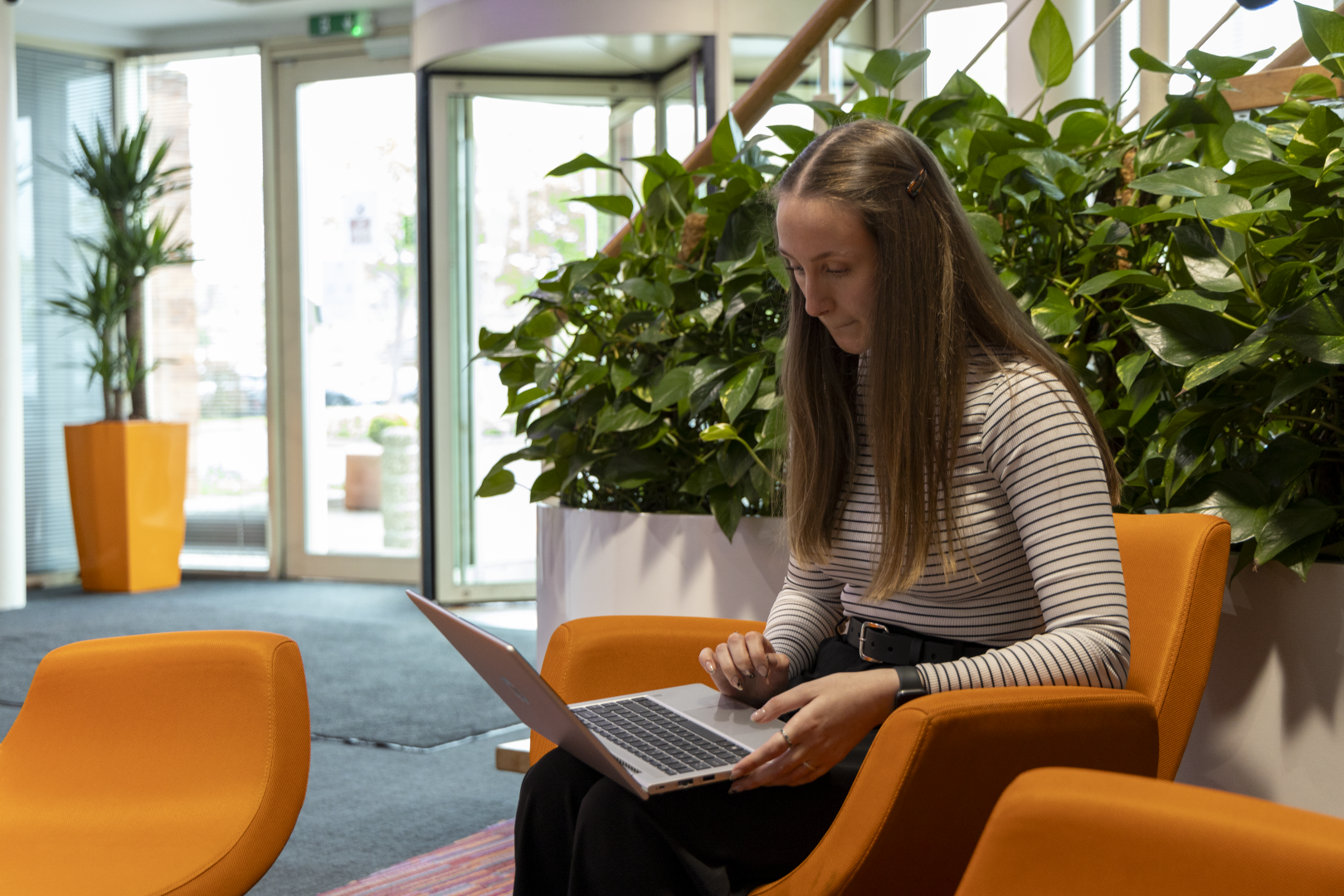 a lady sitting down on a laptop with greenery behind her