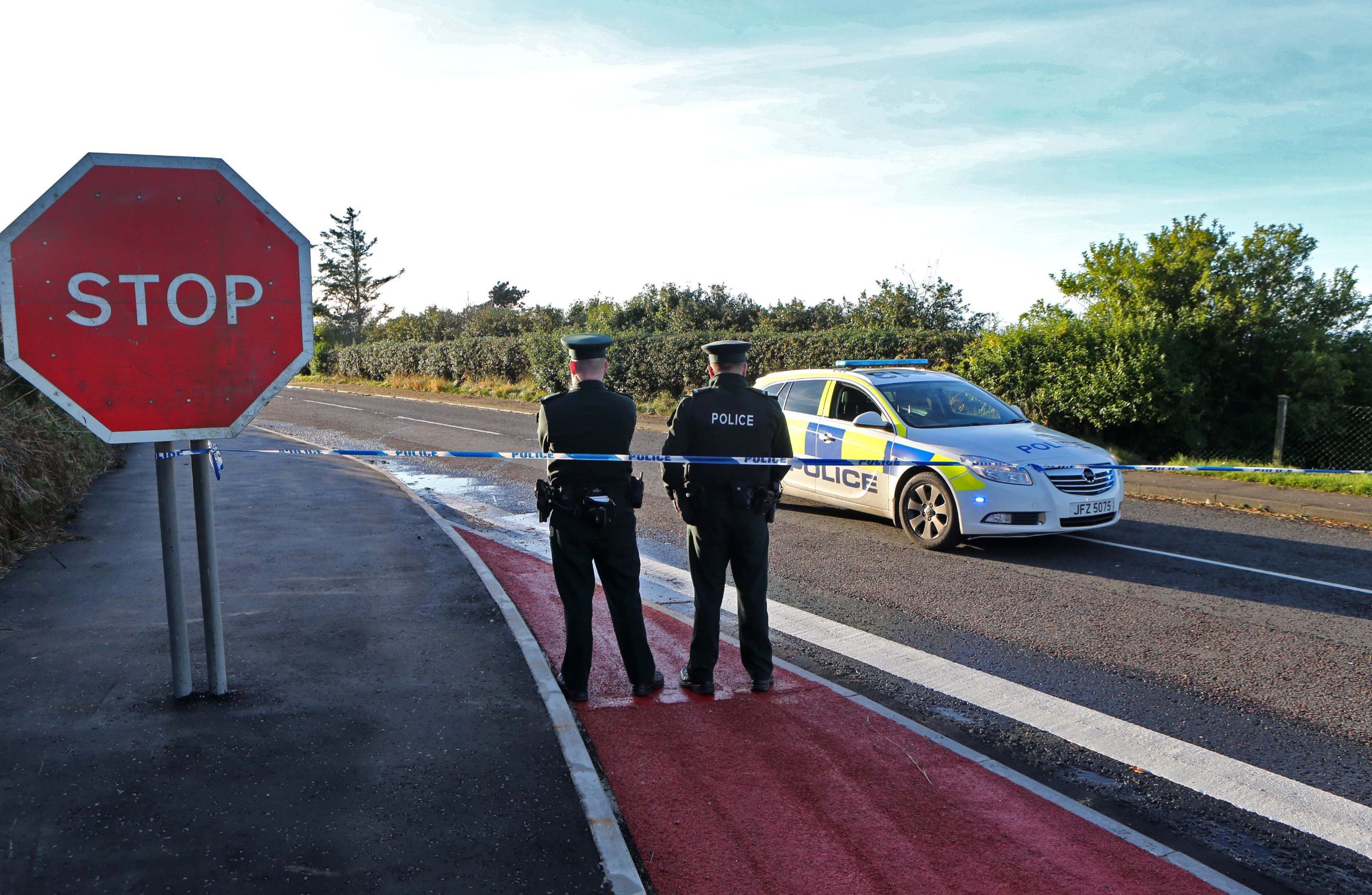Two police men standing with tape across the road.
